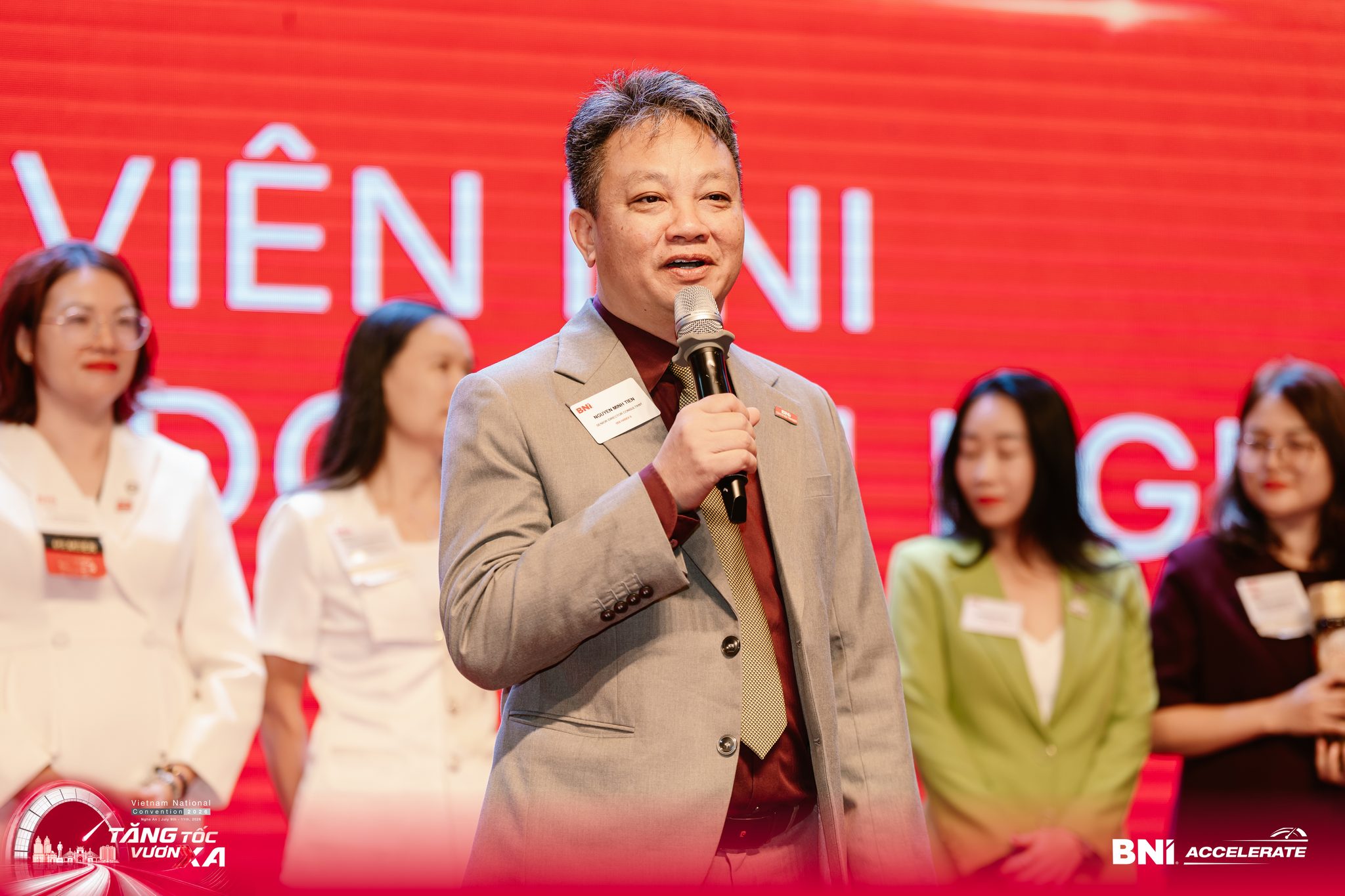 Nguyễn Minh Tiền cầm micro phát biểu trên sân khấu một hội nghị doanh nhân